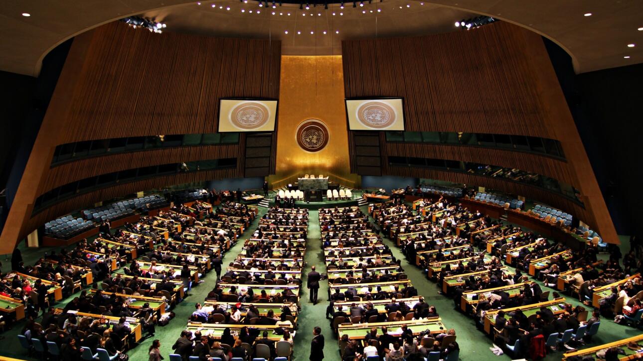 Totale des Generalversammlungssaals der Vereinten Nationen in New York mit goldener Stirnwand, UN-Emblem und Delegiertenreihen