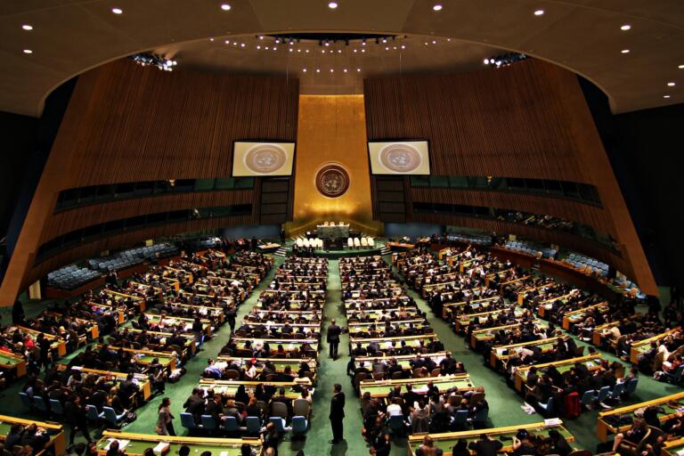 Totale des Generalversammlungssaals der Vereinten Nationen in New York mit goldener Stirnwand, UN-Emblem und Delegiertenreihen